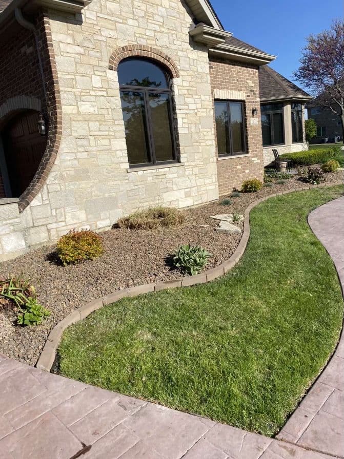Beautiful landscaped front yard with stone accents and curvy garden path beside a brick house.