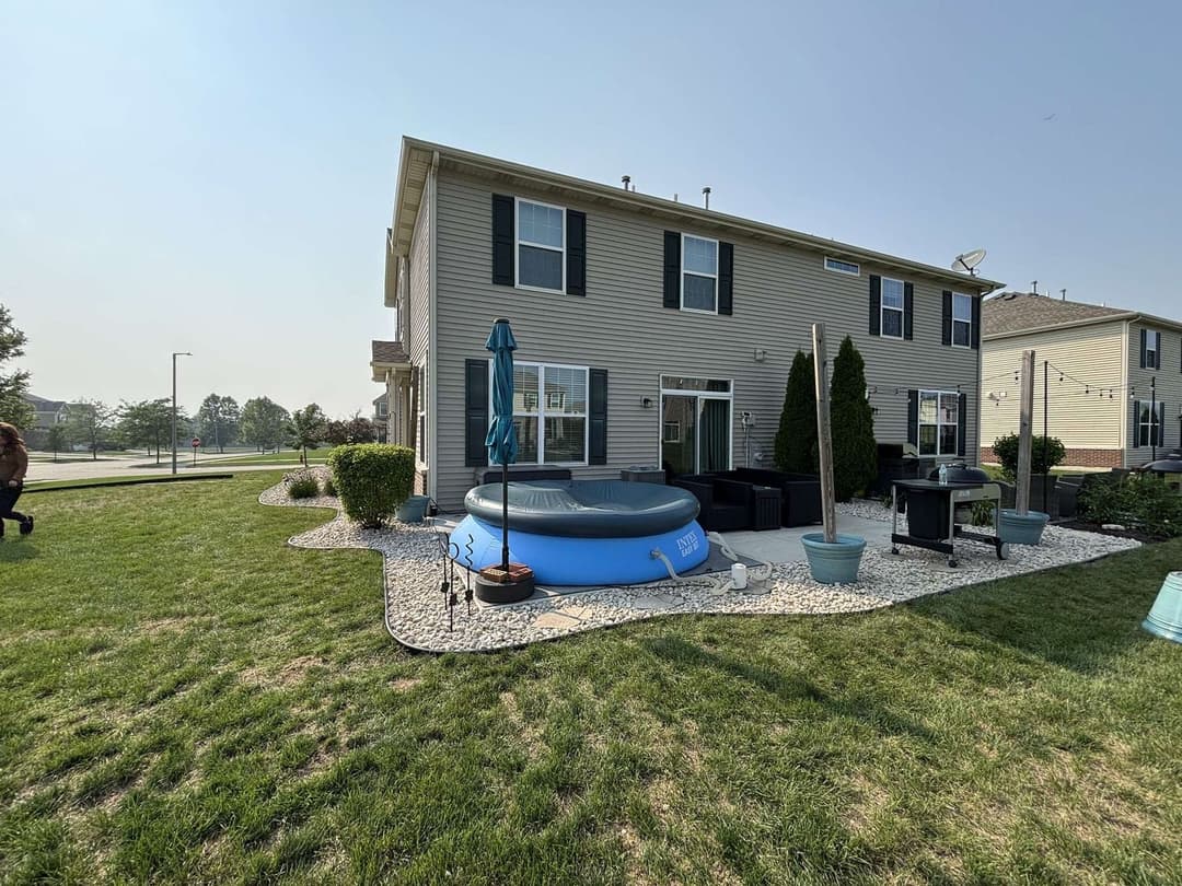 Backyard with above-ground pool, patio furniture, and landscaped grassy area.