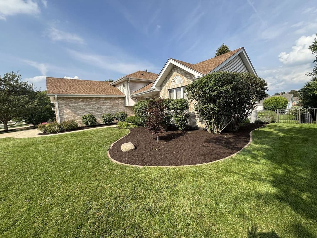 Well-maintained brick home with landscaped garden and green lawn under a blue sky.
