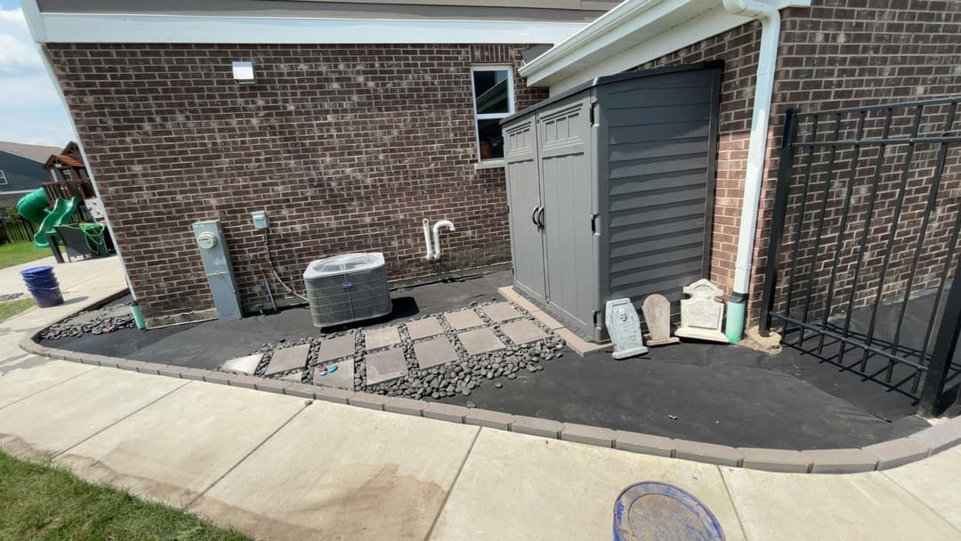 Backyard landscape with a stone pathway, utility shed, air conditioning unit, and black gravel.