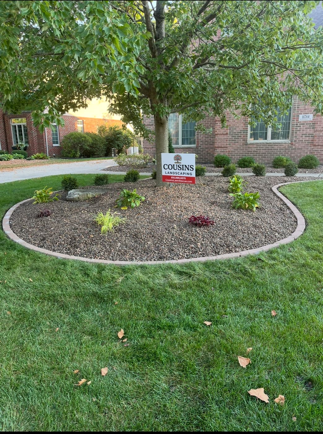 Cousins Landscaping sign in well-maintained flower bed with greenery and gravel at suburban home.
