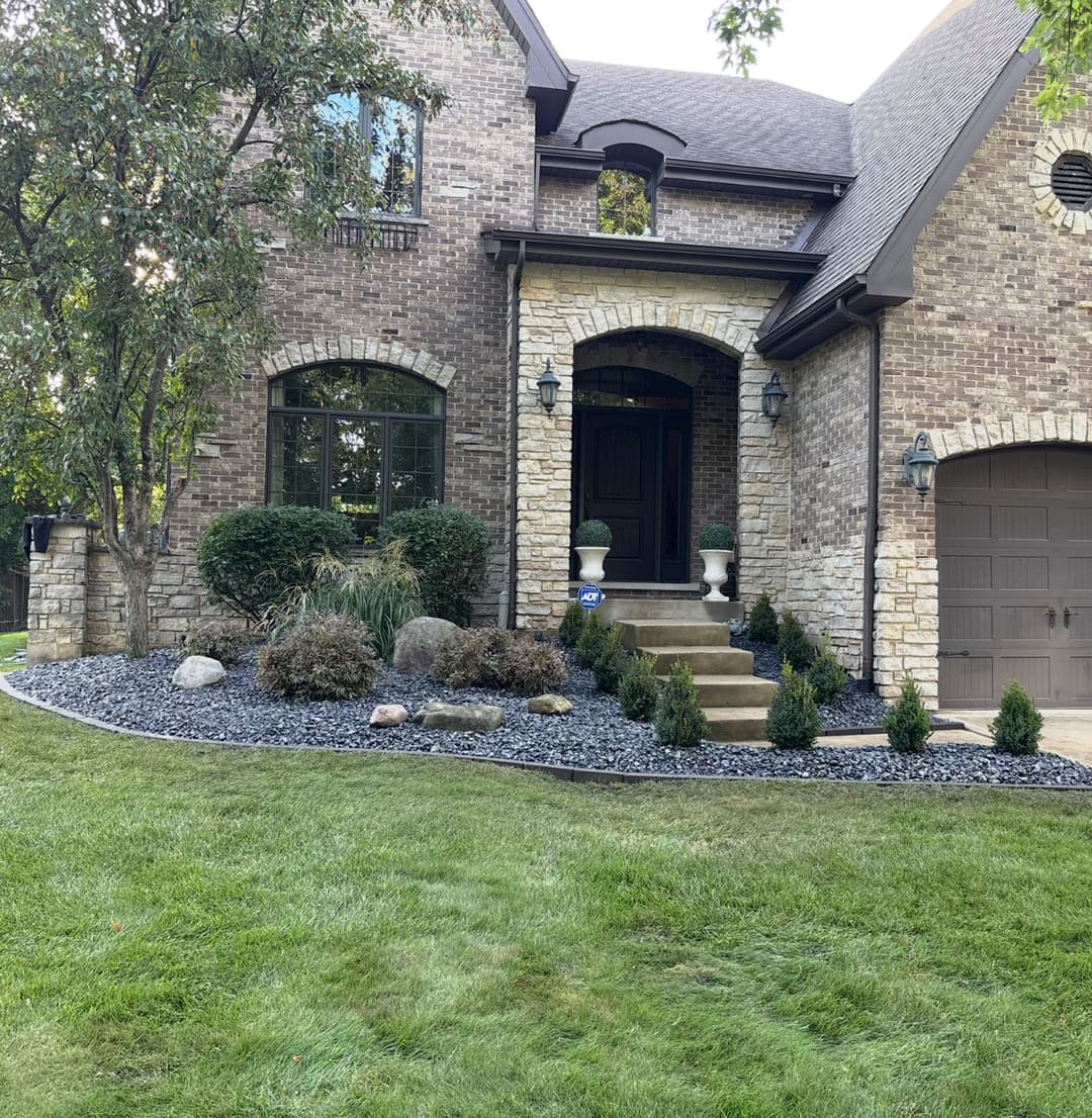 Elegant brick house with stone accents, lush landscaping, and a welcoming front porch.