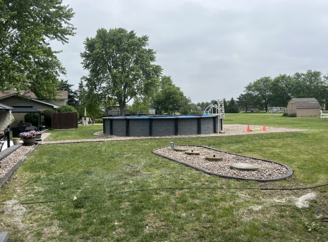Backyard with above-ground pool, grassy area, and landscaping features on a cloudy day.