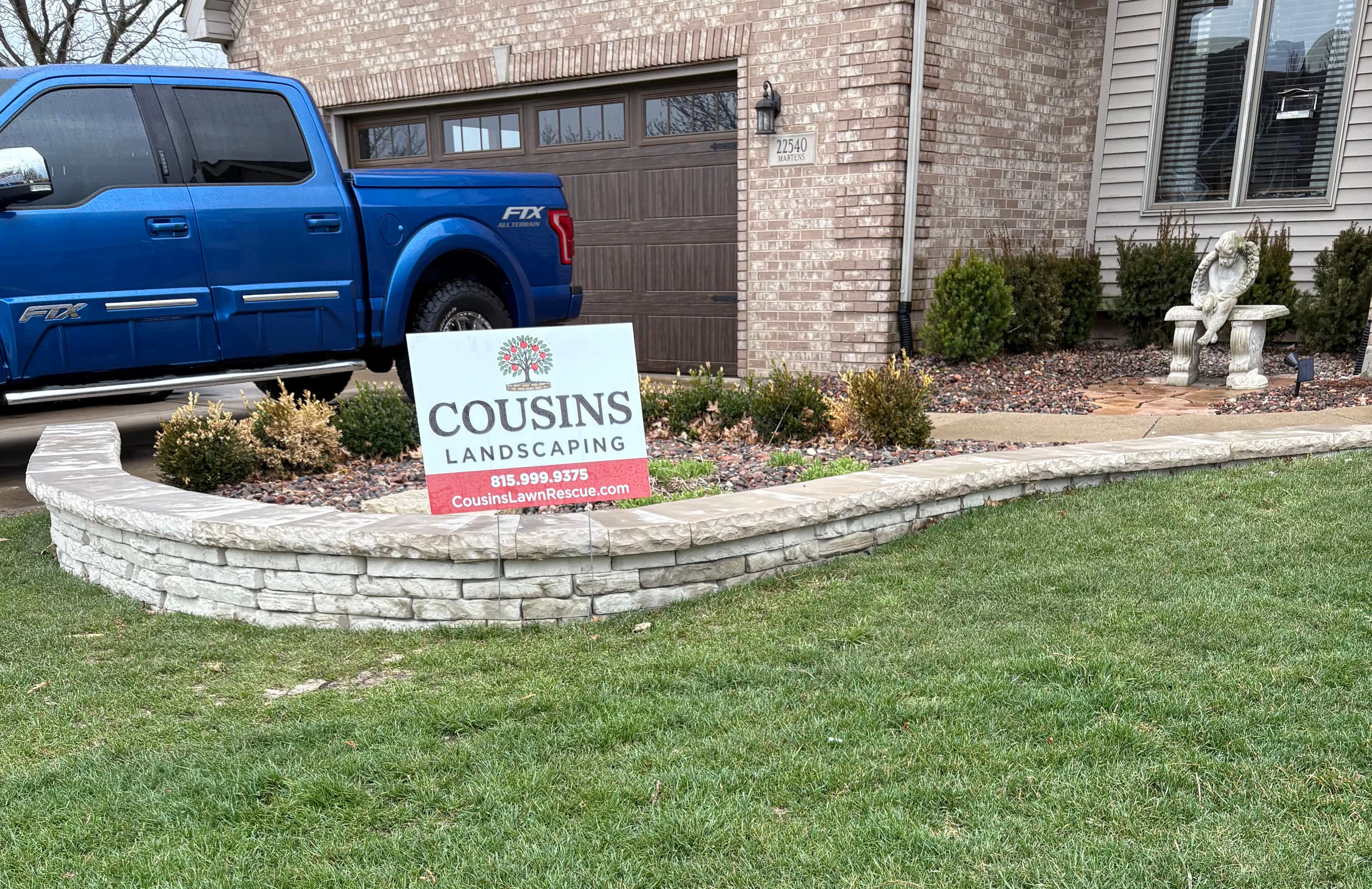 Cousins Landscaping sign near a blue truck and decorative stone landscaping in front yard.