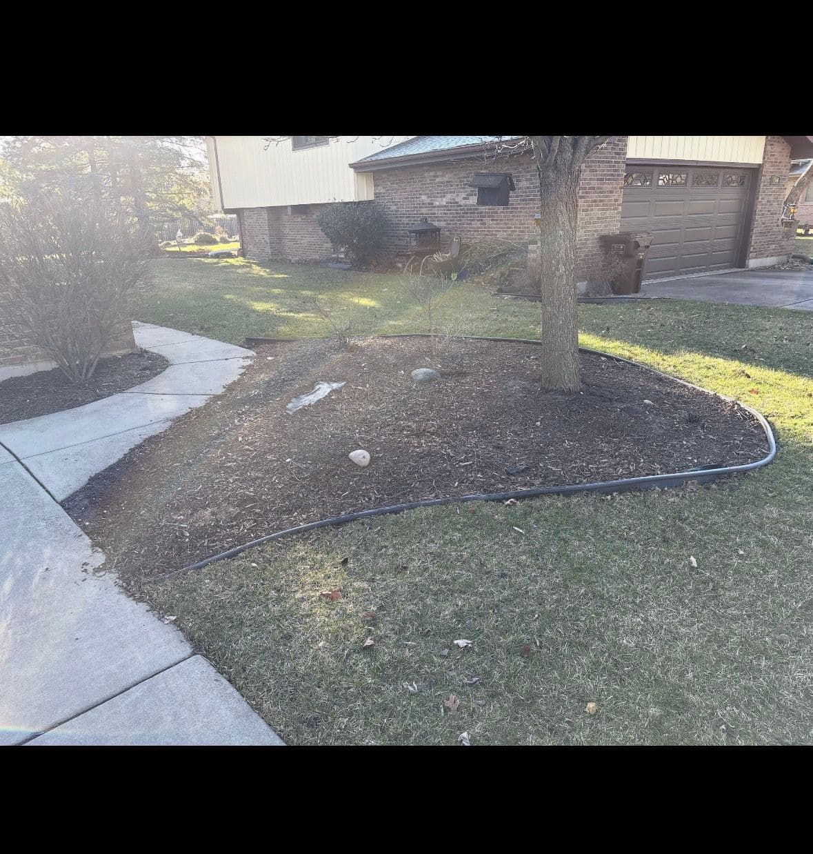 Landscaped yard with mulch, tree, and pathway near a brick house.