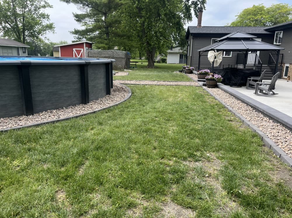 Backyard with a swimming pool, gazebo, and landscaped garden featuring rocks and grass.
