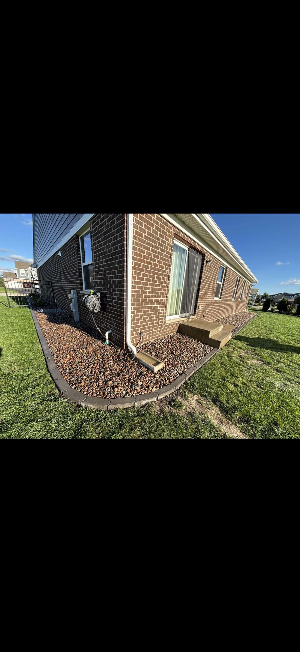 Brick house exterior with landscaped rock border and green lawn under clear blue sky.