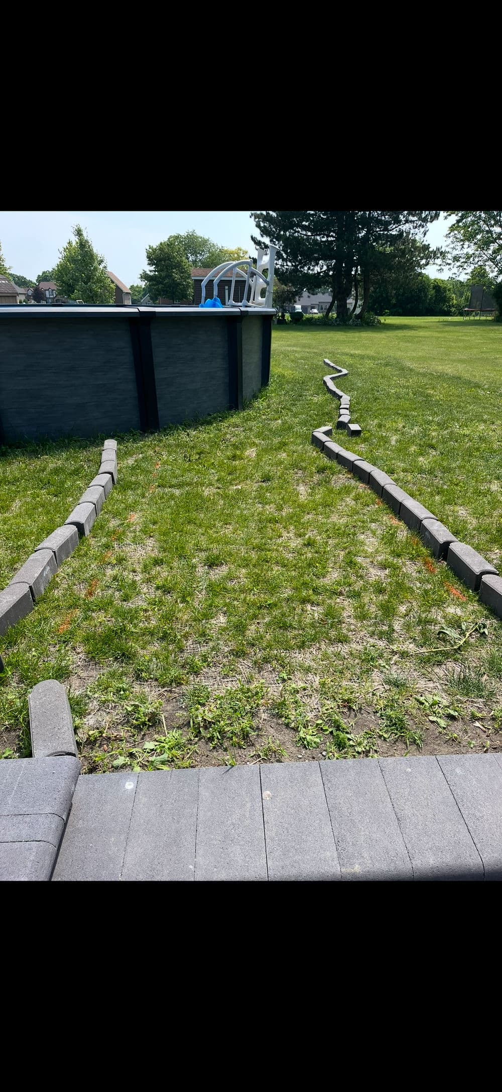 Curved paving stones outline a grassy area leading to an above-ground pool.