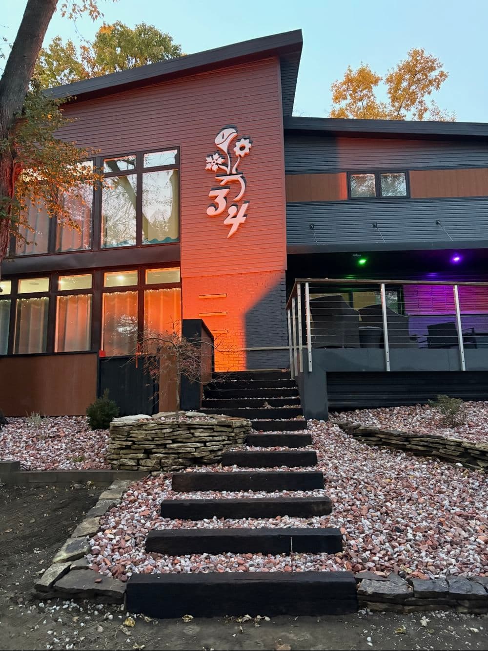 Modern house facade with colorful lighting and landscaped stone pathway. Address: 34.